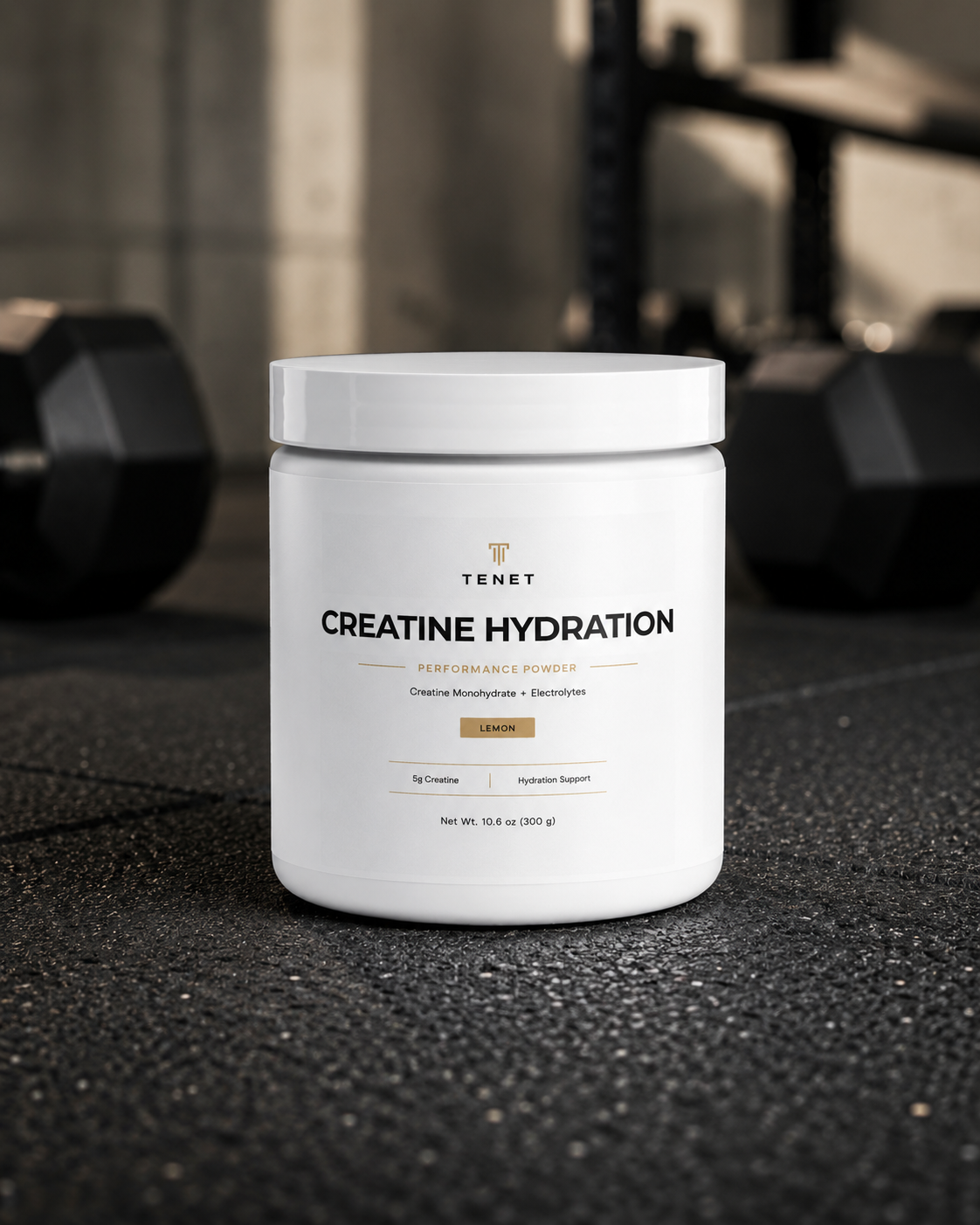 A Tenet Creatine Hydration jar on the floor of a training space, dumbbell rack in the background.